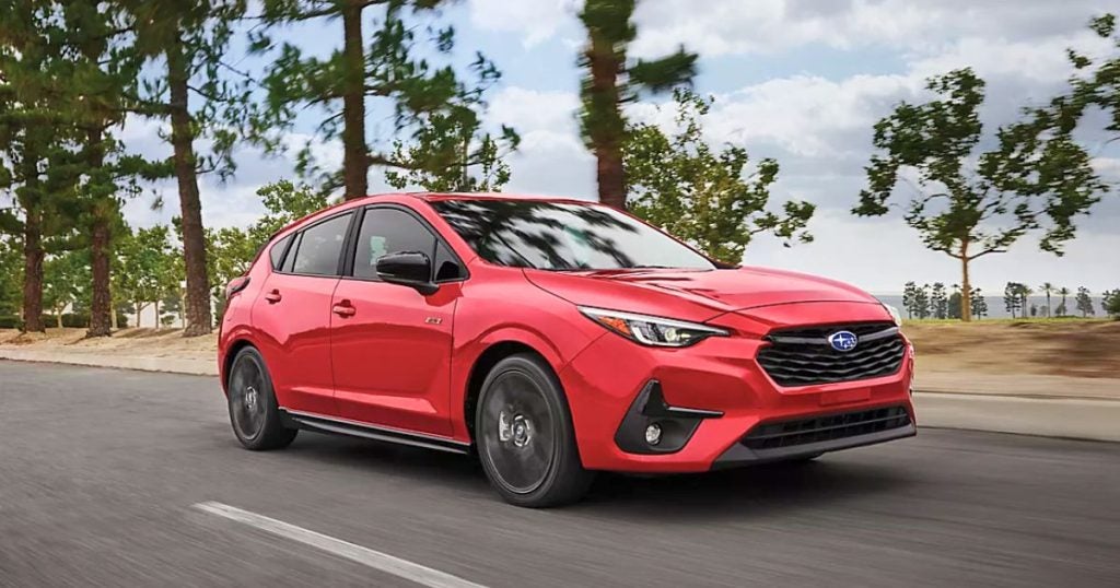 Red 2025 Subaru Impreza hatchback driving on a tree-lined road