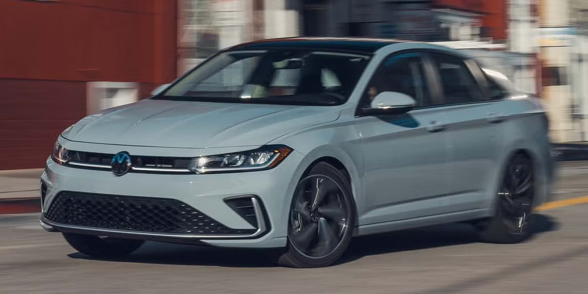 2027 Volkswagen Jetta in light blue driving on a city street, front three-quarter view