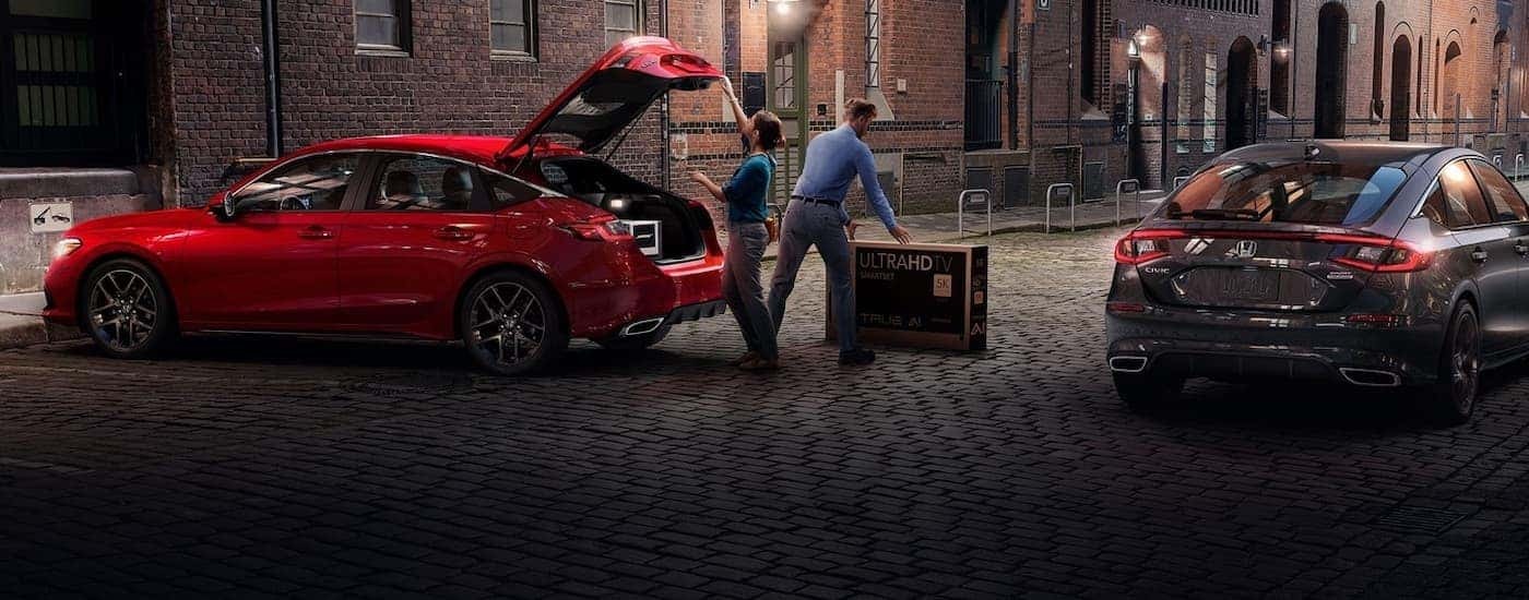 People are shown loading a TV into the trunk of a red 2022 Honda Civic Hatchback.