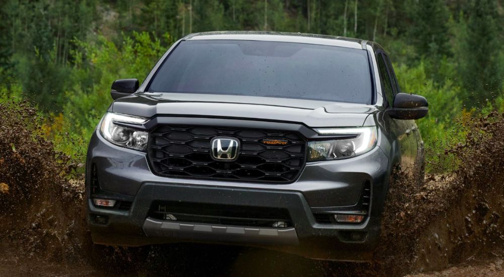 Grey 2026 Honda Ridgeline TrailSport driving off-road through mud.