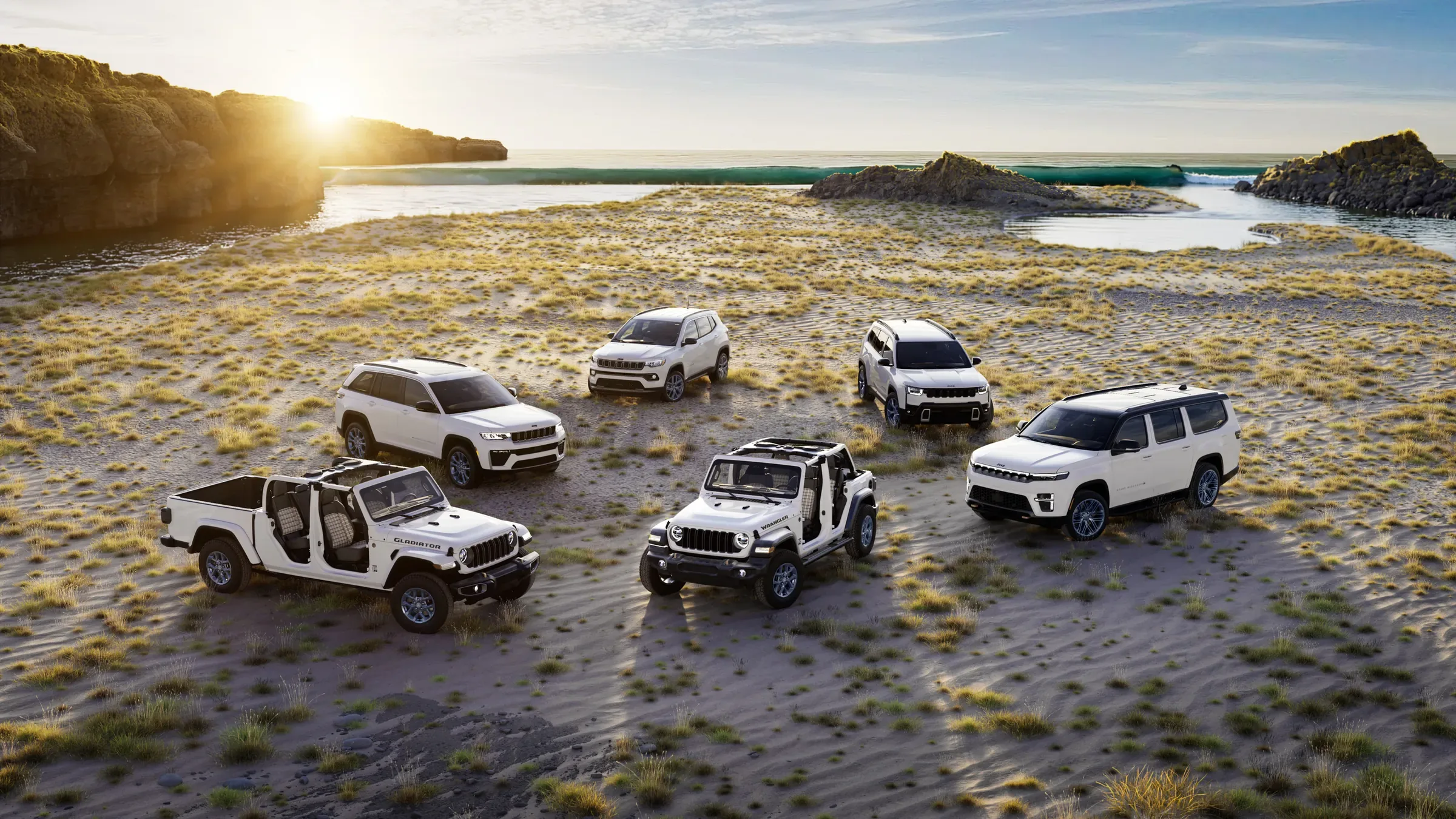 Six Jeep SUVs and trucks, including the Wrangler and Gladiator, parked on a beach at sunset