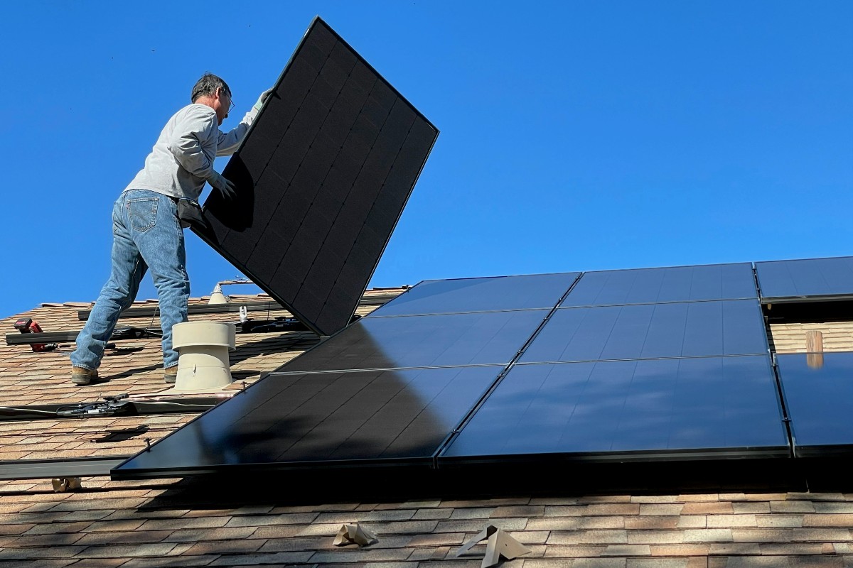 Man Precariously Balancing Solar Panel on Roof