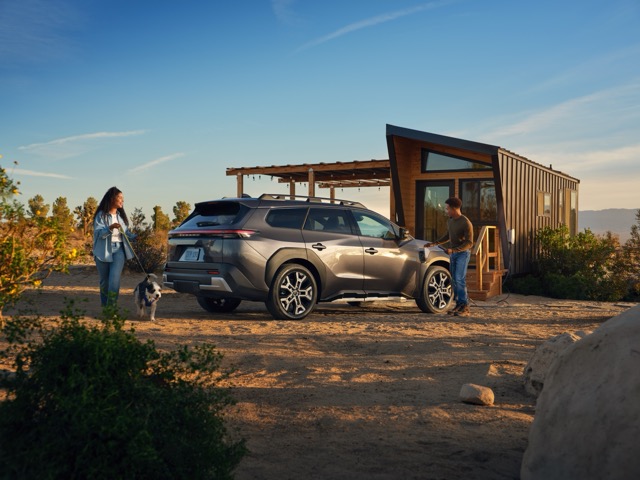 A static image of a grey 2027 Subaru Trailseeker parked on a grassy clearing in a rocky mountain landscape.  