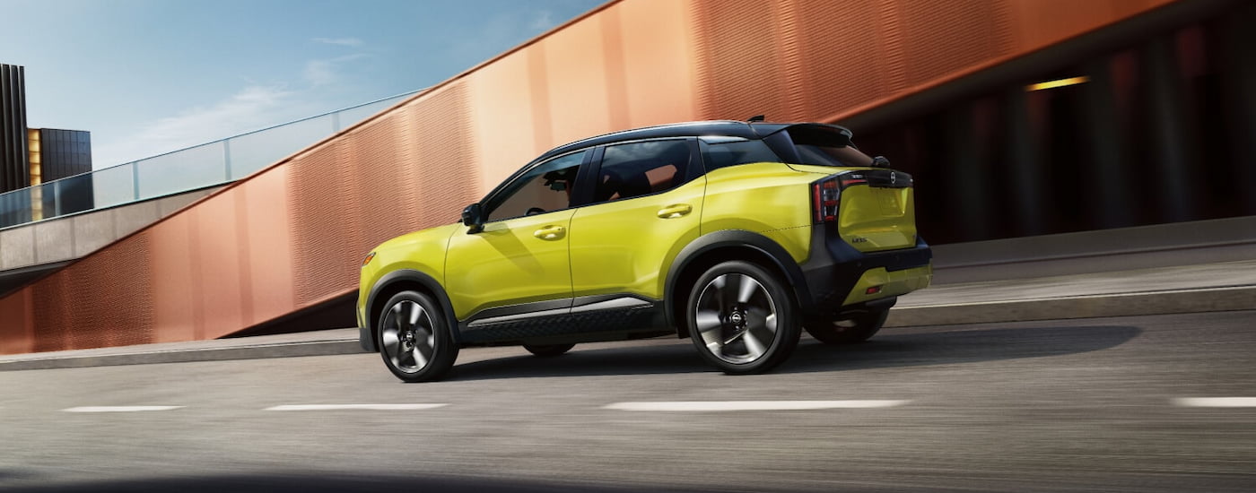 Rear of a yellow 2026 Nissan Kicks SR driving down an open road.
