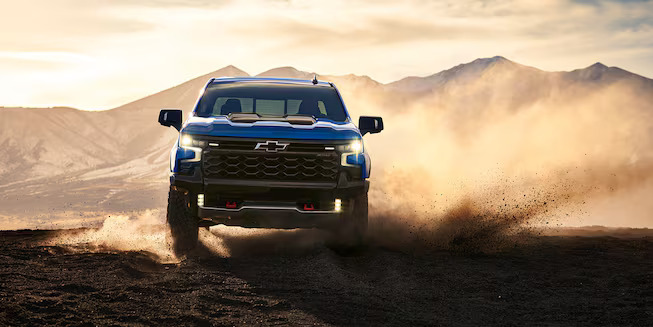 A blue truck driving through the dirt.