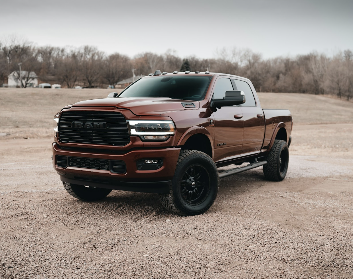 A red-brown Ram pickup truck with black wheels parked on a gravel path.