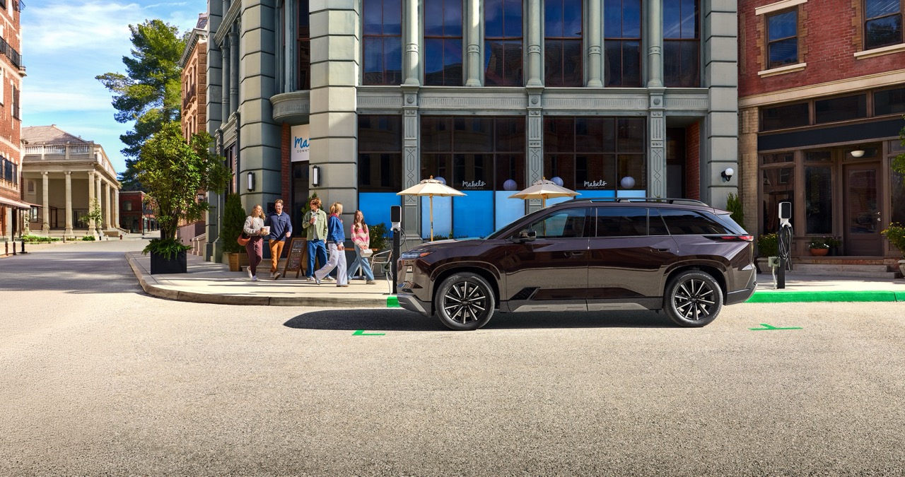 2027 Subaru EV SUV parked at curb outside of urban coffee shop.