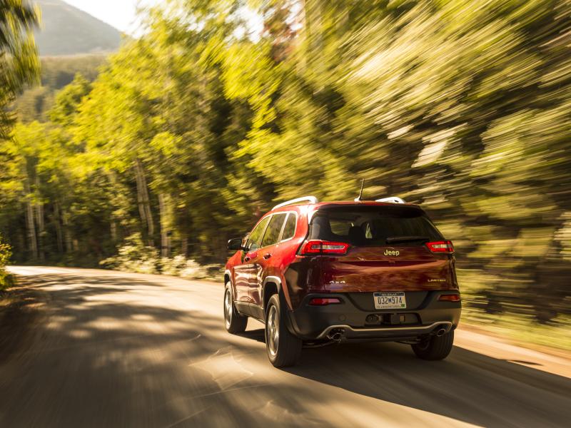 Red Jeep SUV driving fast along a tree-lined road with motion blur