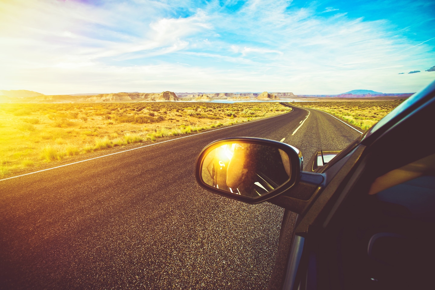 Open desert highway reflected in a car side mirror at sunset