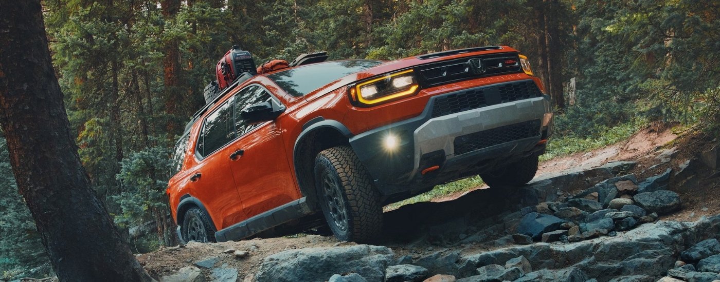 An orange 2026 Honda Passport TrailSport Elite driving a trail.