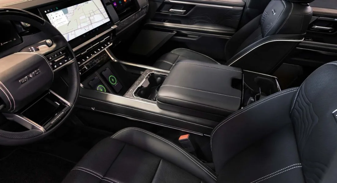 Close-up of a GMC vehicle's center console showing two phones charging on wireless charging pads with illuminated indicator lights, a column-mounted shifter, and a navigation map on the touchscreen display