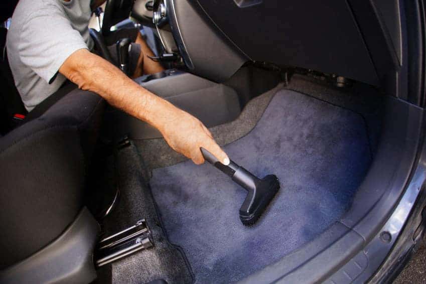 Detailer vacuuming car floor carpet