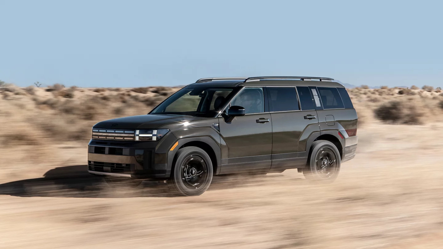 A green suv driving on a dirt road.