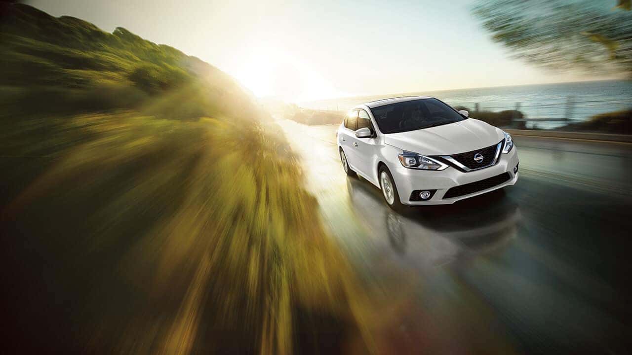 White 2017 Nissan Sentra driving on a coastal road at sunset