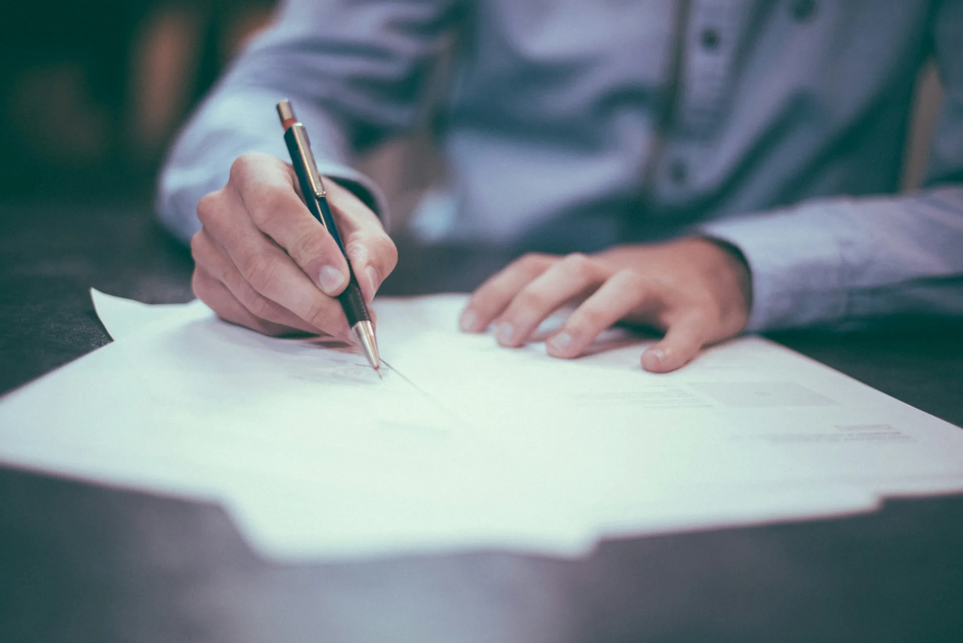 Close-up of a hand signing a document with a pen at a desk